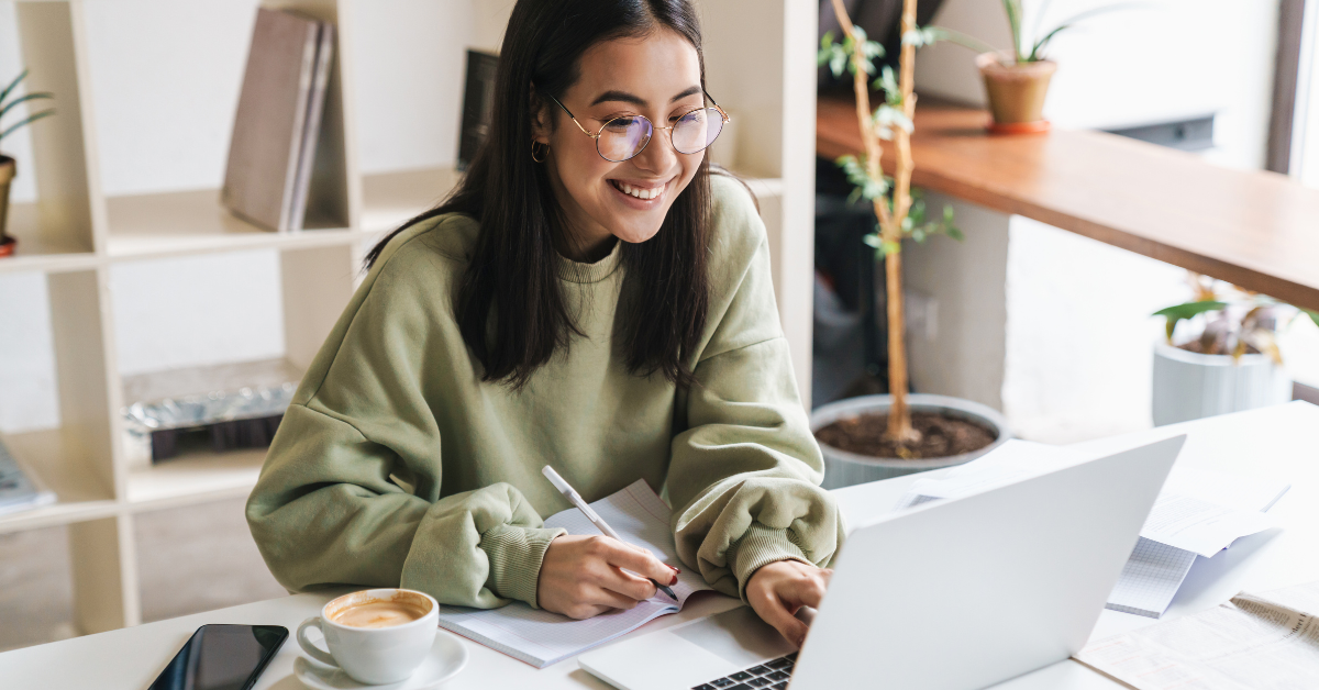 young woman wearing glasses and green sweater smiling on laptop