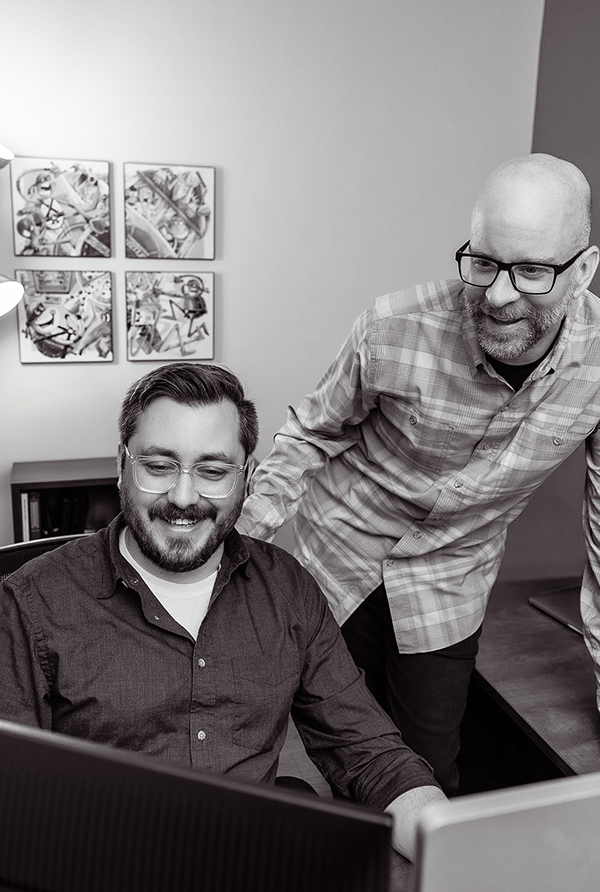 Graphic designers, Drew and Mark. looking at a computer screen together.