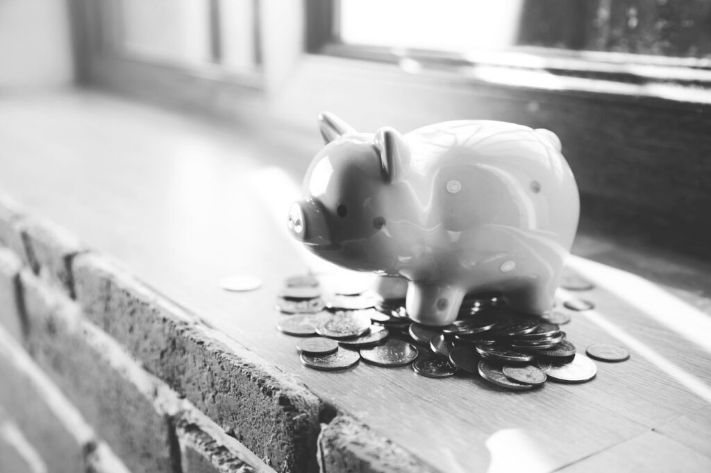 Piggy bank sitting on a windowsill ledge beside scattered coins